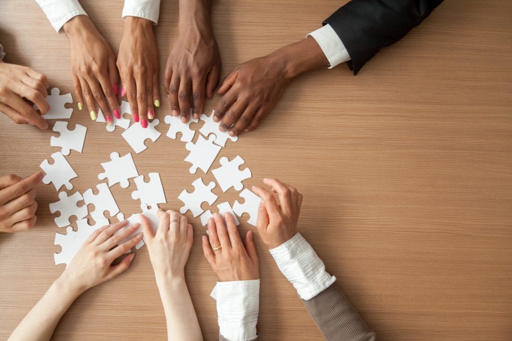 Hands of multi-ethnic business team assembling jigsaw puzzle, to